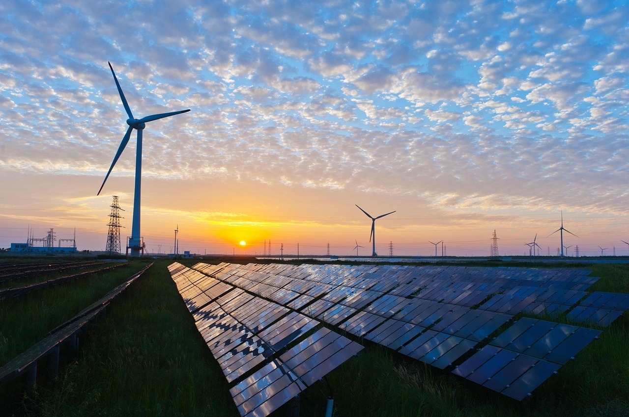 Renewable energy farm at sunset featuring solar panels in the foreground and wind turbines in the background, symbolizing sustainable power solutions and environmental innovation.