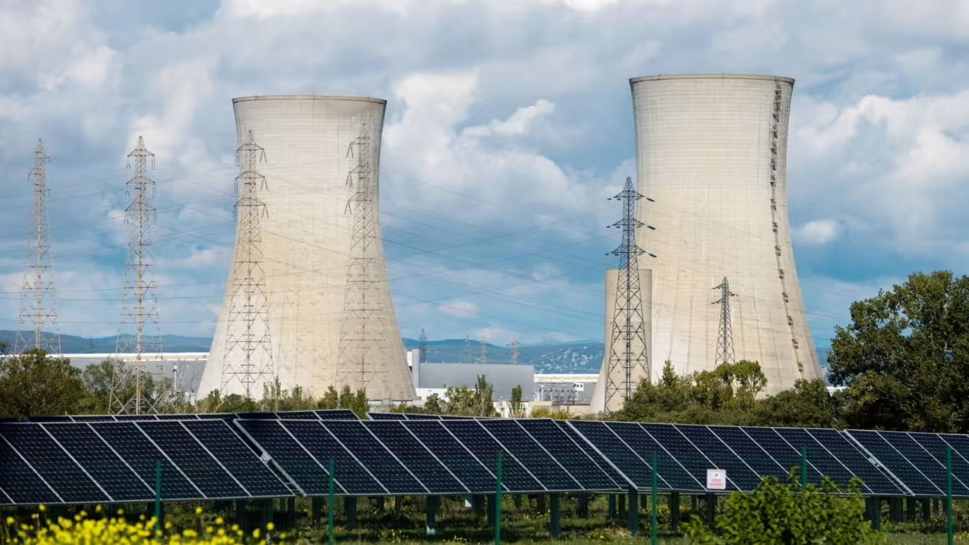 Thumbnail image for the 'Energizing Australia: Renewable Versus Nuclear in the National Debate' article, featuring a solar panel farm in the foreground with large nuclear power plant cooling towers in the background, visually representing the contrast and discussion points between renewable and nuclear energy options discussed in the summary of the Moolah show hosted by Omar de Silva.