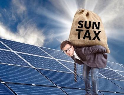 Man carrying a heavy 'Sun Tax' sack in front of solar panels, illustrating the financial burden of new solar levies on homeowners and businesses.