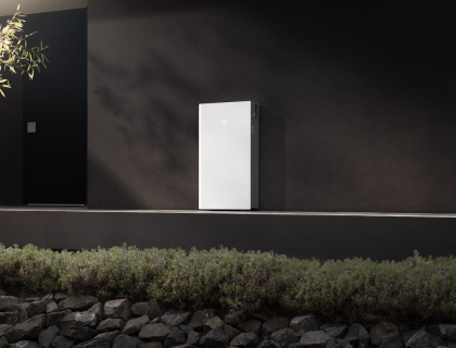 Tesla Powerwall 3P mounted on a dark exterior wall in afternoon sun